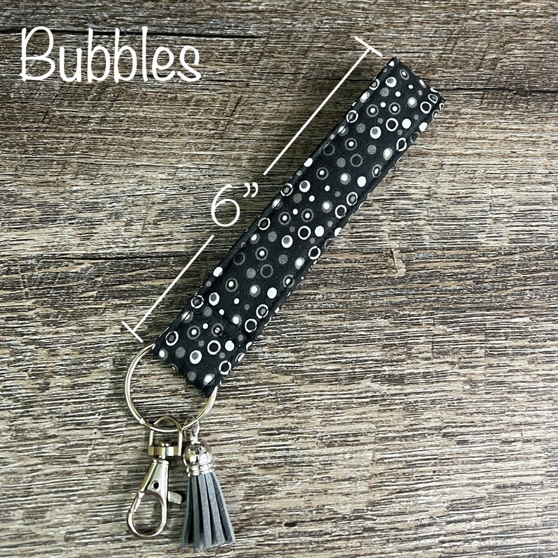 May include: A black and white fabric key chain with a gray tassel and a silver key ring. The fabric has a pattern of white circles on a black background. The key chain is 6 inches long.