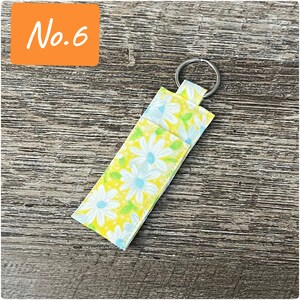 May include: A yellow and white floral key chain with a silver ring. The key chain is made of fabric and has a daisy pattern.