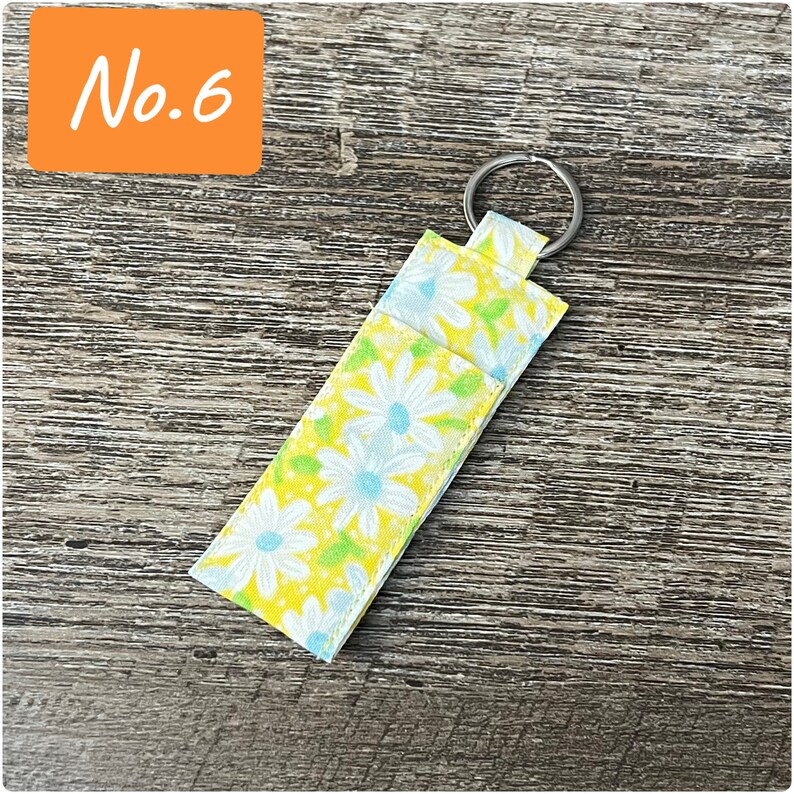 May include: A yellow and white floral key chain with a silver ring. The key chain is made of fabric and has a daisy pattern.