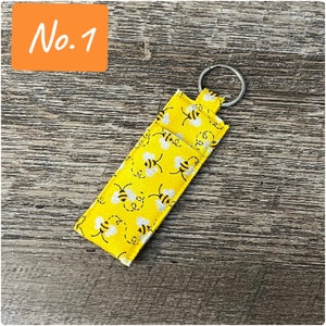 May include: A yellow fabric keychain with a silver ring and a bee pattern. The keychain has the text "No. 1" printed on it.