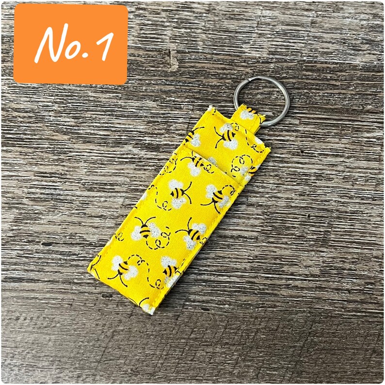 May include: A yellow fabric keychain with a silver ring and a bee pattern. The keychain has the text "No. 1" printed on it.