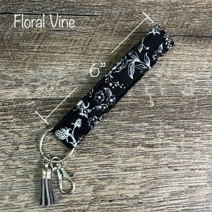 May include: Black and white floral patterned key chain with a gray tassel and a silver key ring. The key chain is 6 inches long.