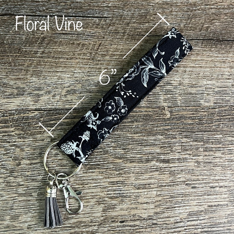 May include: Black and white floral patterned key chain with a gray tassel and a silver key ring. The key chain is 6 inches long.