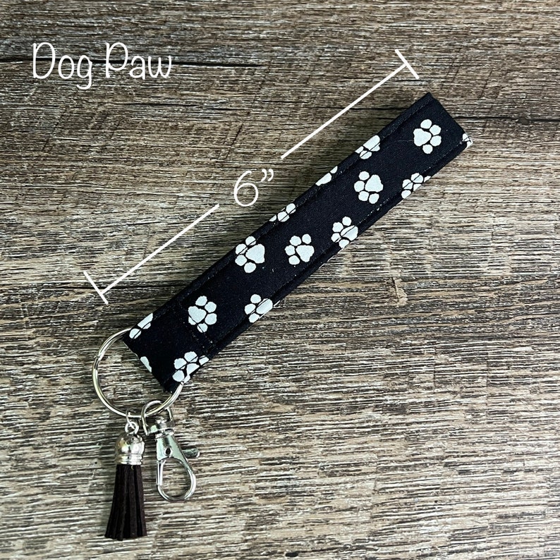 May include: Black key chain with a white paw print pattern and a brown tassel. The key chain is 6 inches long.