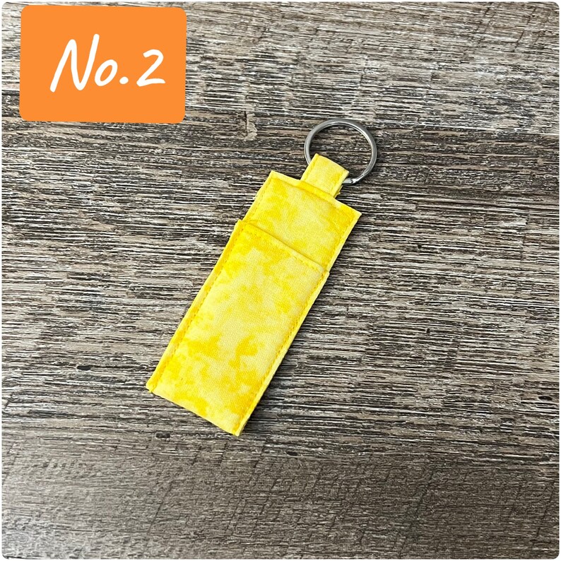 May include: A yellow fabric key chain with a single key ring. The fabric has a light yellow tie-dye pattern.