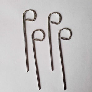 May include: Four silver metal hooks with a rounded loop at the top. The hooks are straight and have a smooth finish.
