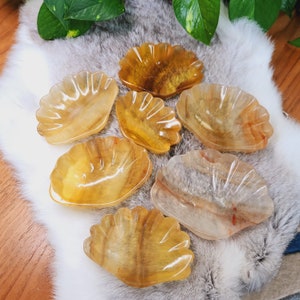 May include: Six yellow calcite crystal dishes in various shapes and sizes. The dishes are arranged on a white faux fur surface.