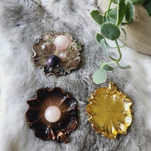 May include: Three decorative dishes with a floral design. The dishes are made of metal and have a gold, silver, and copper finish. The dishes are perfect for holding small items, such as jewelry or crystals.