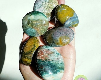 May include: A collection of seven polished ocean jasper stones, each with unique swirling patterns of green, blue, brown, and white. The stones are smooth and have a natural, organic look.