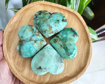 Peut inclure: Quatre pierres de turquoise en forme de cœur, vertes et bleues, sur un plateau en bois.