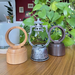 May include: Three decorative lamp bases on a wooden surface. The left base is light wood with a circular top. The center base is a silver-toned metal lantern shape with scrollwork. The right base is dark wood with a circular top.