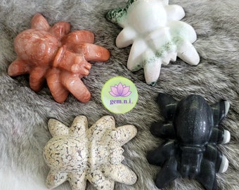 May include: Four carved stone spider sculptures in different colors and patterns. The spiders are made of red, white, green, and black stone.