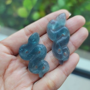 Puede incluir: Dos tallas de jade azul verdoso de un diseño de serpiente en un nudo. Las tallas son lisas y pulidas.
