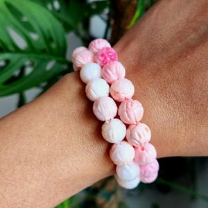 Peut inclure: Deux bracelets en perles de corail rose avec des motifs floraux sculptés. Les perles sont graduées en taille, les plus grosses au centre du bracelet et les plus petites aux extrémités.