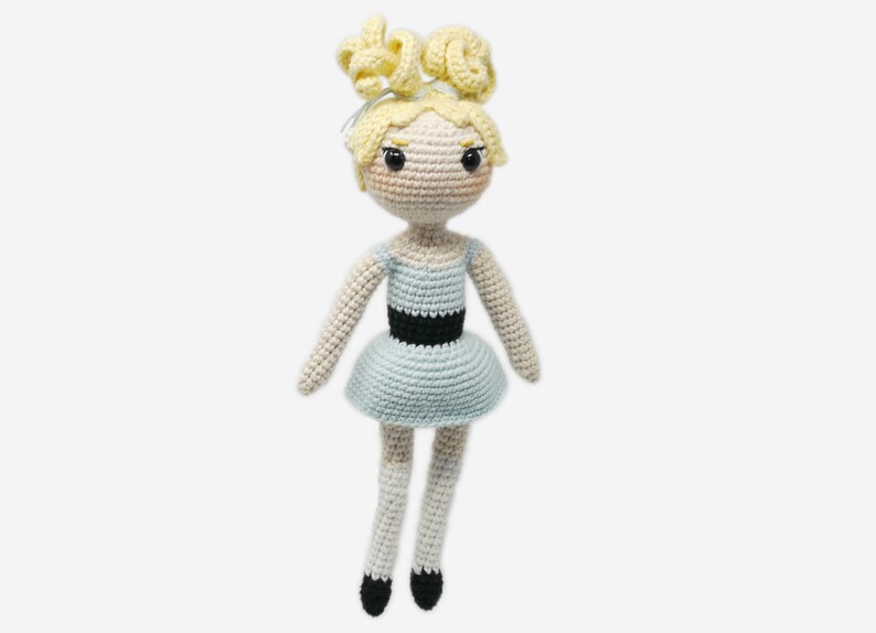 May include: A crocheted doll with blonde hair, a light blue dress with a black belt, and white socks and black shoes.