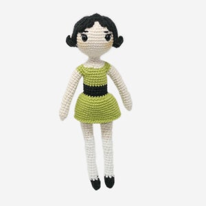 May include: A crocheted doll with black hair, green dress, and white legs. The doll has a black belt and black shoes.