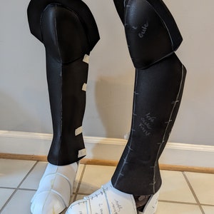 May include: Two black foam leg pieces for a costume. The pieces are marked with handwritten notes, including "left calf front" and "outer".