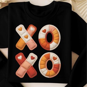 Könnte beinhalten: Schwarzes Sweatshirt mit einem gesteppten "XO"-Design. Die "X"s sind in Orange, Rosa und Weiß mit Herzdetails. Die "O"s sind in Orange, Weiß und Rosa mit Herzdetails. Ein bequemes und modisches Oberteil.