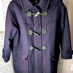 May include: A dark purple duffel coat with a classic design. The coat features a collared neckline, toggle closures, and two front pockets. The toggle closures are made of wood and leather.
