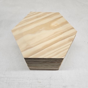 May include: A stack of hexagonal wooden pieces, each with a light wood grain pattern. The pieces are stacked to form a hexagonal shape.