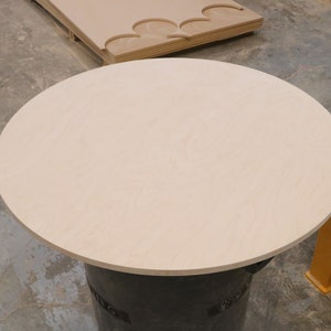 May include: A round, light-colored wood tabletop, approximately 30 inches in diameter, sits on a black base.