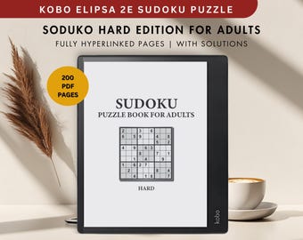 May include: A black and white e-reader with a white screen displaying a Sudoku puzzle book for adults. The screen shows the text "Sudoku Puzzle Book for Adults" and a sample Sudoku puzzle labeled "Hard". The e-reader has a black bezel and the text "kobo" is visible on the bottom right corner. The e-reader is sitting on a white surface with a brown plant and a cup of coffee in the background.