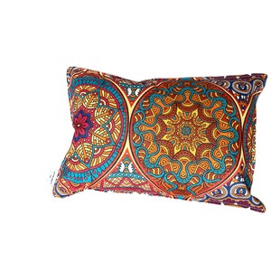 Può includere: Un cuscino decorativo con un motivo a mandala colorato in tonalità di arancione, blu, giallo e rosso. Il cuscino è rettangolare e ha una consistenza morbida e soffice.