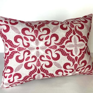 Puede incluir: Una almohada de tiro roja y blanca con un diseño geométrico. La almohada está hecha de una tela suave y texturizada.