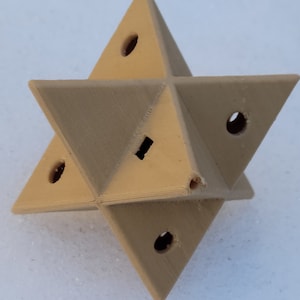 May include: A beige 3D printed star-shaped object with six points and five holes. The object is made of a smooth, matt material.