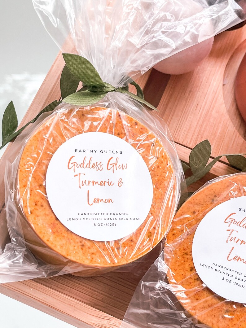 May include: Two round bars of handmade goat milk soap wrapped in clear plastic. The soap is a vibrant orange color and has a white label that reads "Goddess Glow Turmeric & Lemon" and "Handcrafted Organic Lemon Scented Goats Milk Soap 5 oz (142g)".