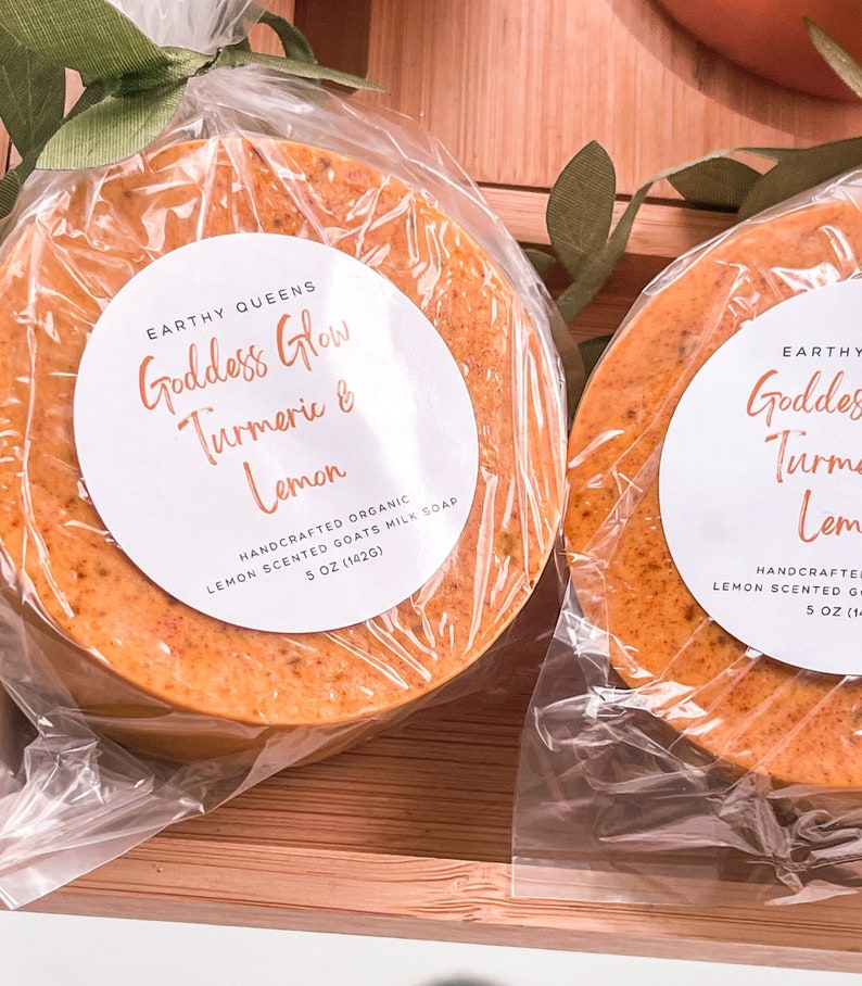 May include: Two round bars of handmade organic goats milk soap wrapped in clear plastic with a white label that reads "Earthy Queens Goddess Glow Turmeric & Lemon Handcrafted Organic Lemon Scented Goats Milk Soap 5 oz (142g)"