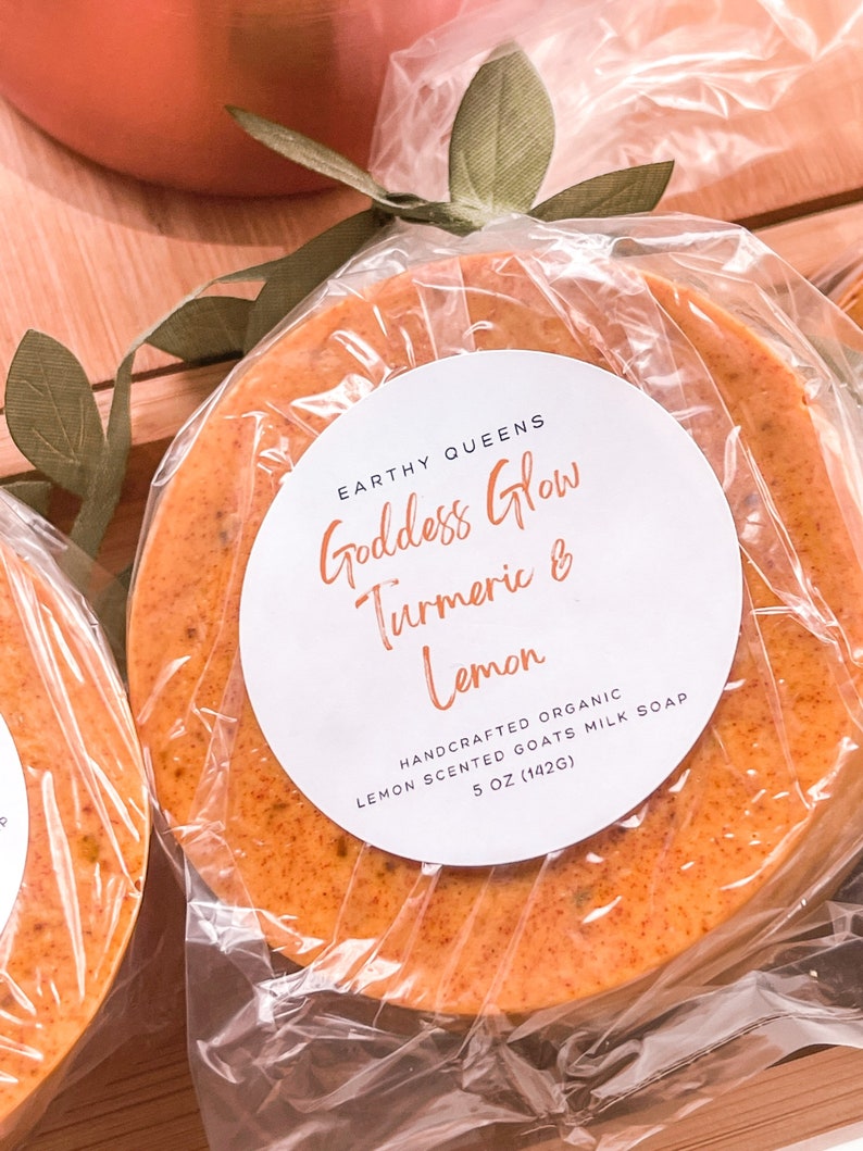 May include: A round, orange-colored goat milk soap bar with a white label that reads "Goddess Glow Turmeric & Lemon" and "Handcrafted Organic Lemon Scented Goats Milk Soap 5 oz (142g)".