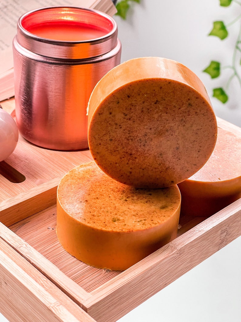 May include: Three round orange-brown soap bars on a wooden tray. The soap bars are stacked on top of each other.