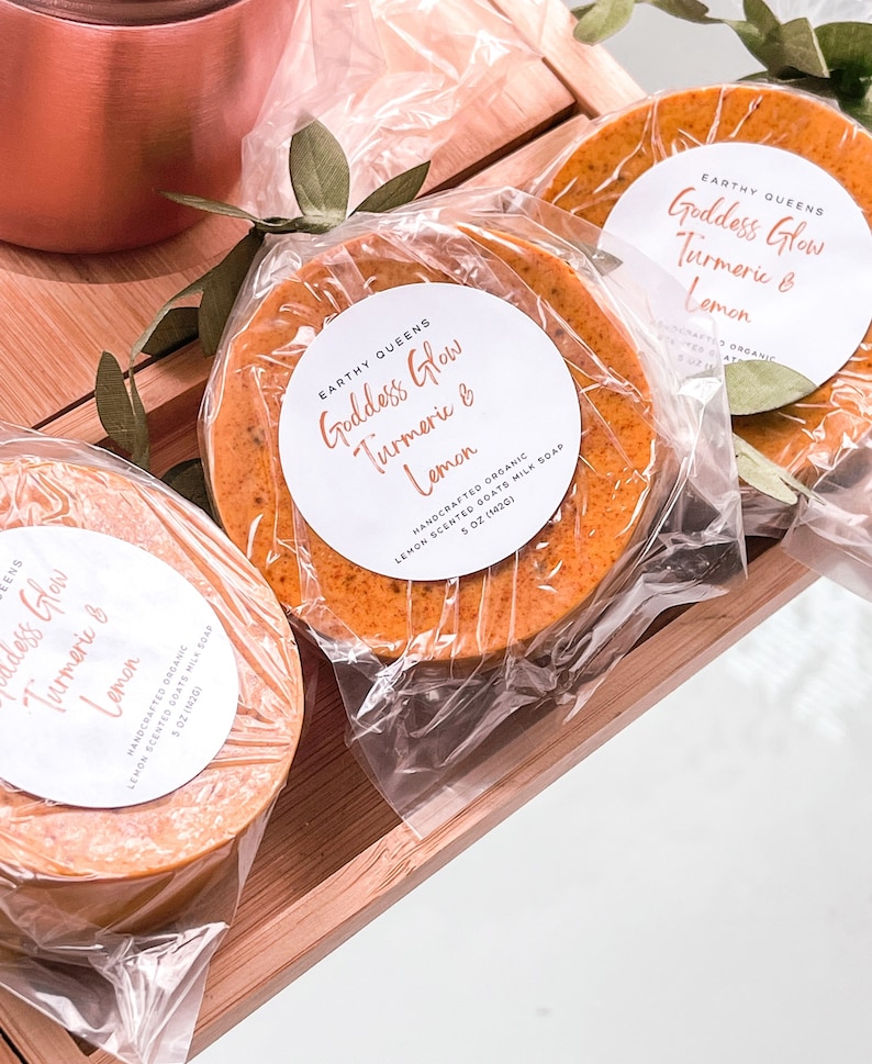 May include: Three bars of handmade soap wrapped in plastic. The soap is a bright orange color and has a label that says "Goddess Glow Turmeric & Lemon" with the words "Handcrafted Organic Lemon Scented Goats Milk Soap 5 oz (142g)".