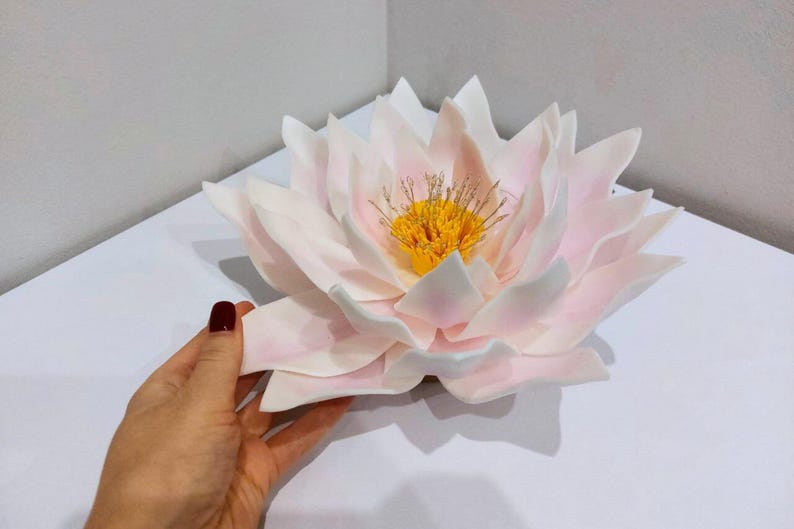 May include: A large, white and pink paper flower resembling a water lily. The flower has a yellow center with a delicate, intricate design.