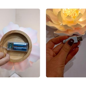 May include: A white flower-shaped lamp with a wooden base and a battery compartment. The lamp is lit and has a warm glow. The lamp can also be powered by a USB cable.