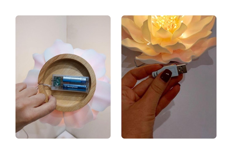 May include: A white flower-shaped lamp with a wooden base and a battery compartment. The lamp is lit and has a warm glow. The lamp can also be powered by a USB cable.
