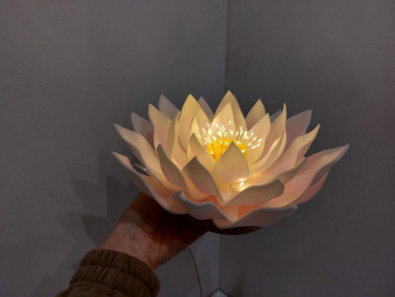May include: A white paper flower with a yellow center and a string of lights inside. The flower is lit up and looks like a lotus flower.