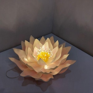 May include: A white paper lotus flower with a yellow center and a string of lights inside. The flower is lit up and glowing.