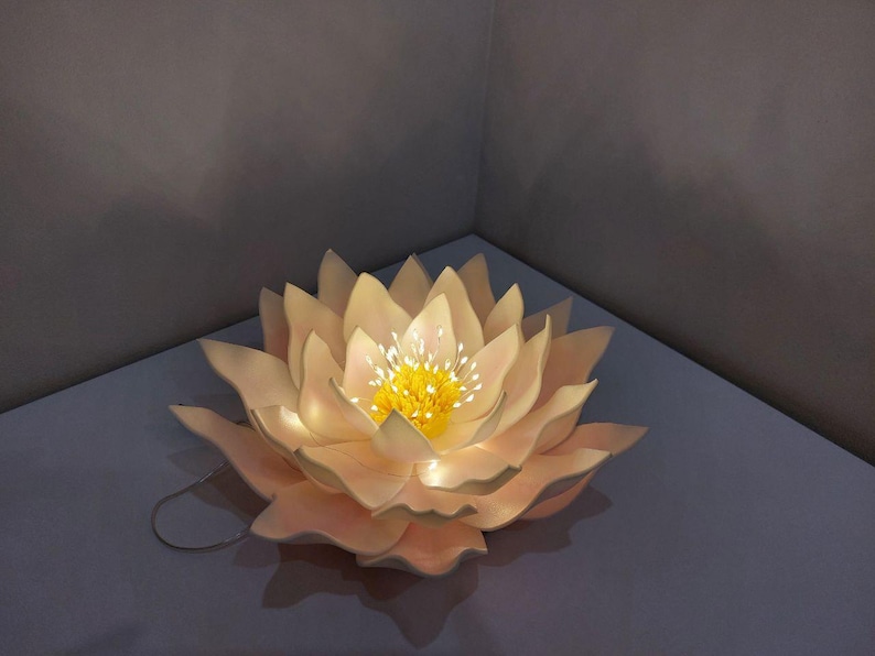 May include: A white paper lotus flower with a yellow center and a string of lights inside. The flower is lit up and glowing.