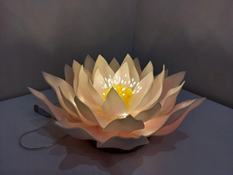 May include: A white, paper-like lotus flower lamp with a yellow center and white lights. The lamp is lit and casting a warm glow.