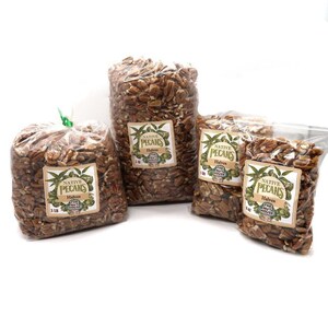 May include: Three bags of pecan halves, each with a label that reads "Native Pecans Halves The Nut House". The bags are clear plastic and the pecans are a light brown color. The bags are arranged in a row from largest to smallest, with the largest bag being 3 pounds, the middle bag being 1 pound, and the smallest bag being 1/2 pound.