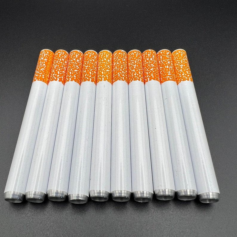 May include: A set of 12 white cigarette-shaped tubes with orange tips. The tubes are arranged in a row on a black surface.