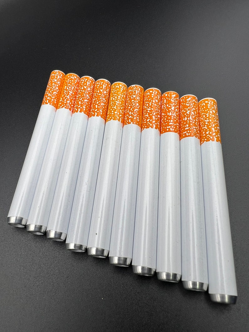 May include: A set of 10 white metal cigarette-shaped pipes with orange tips. The pipes are arranged in a row, with the tips facing the viewer.