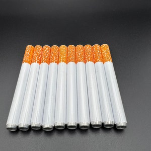 May include: A set of ten white and orange cigarette-shaped pipes. The pipes are arranged in a row on a black surface.