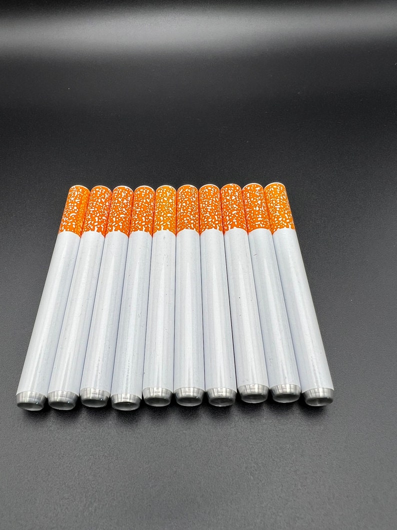 May include: A set of ten white and orange cigarette-shaped pipes. The pipes are arranged in a row on a black surface.