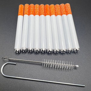 Könnte beinhalten: Ein Satz von zehn weißen zigarettenförmigen Röhrchen mit orangenen Spitzen und einer Reinigungsbürste. Die Röhrchen haben einen gezackten Rand am Ende.