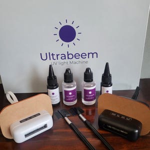 May include: A white UV light machine with a digital timer display, two black brushes, and four bottles of clear liquid labeled "Ultrabeam UV light Machine".