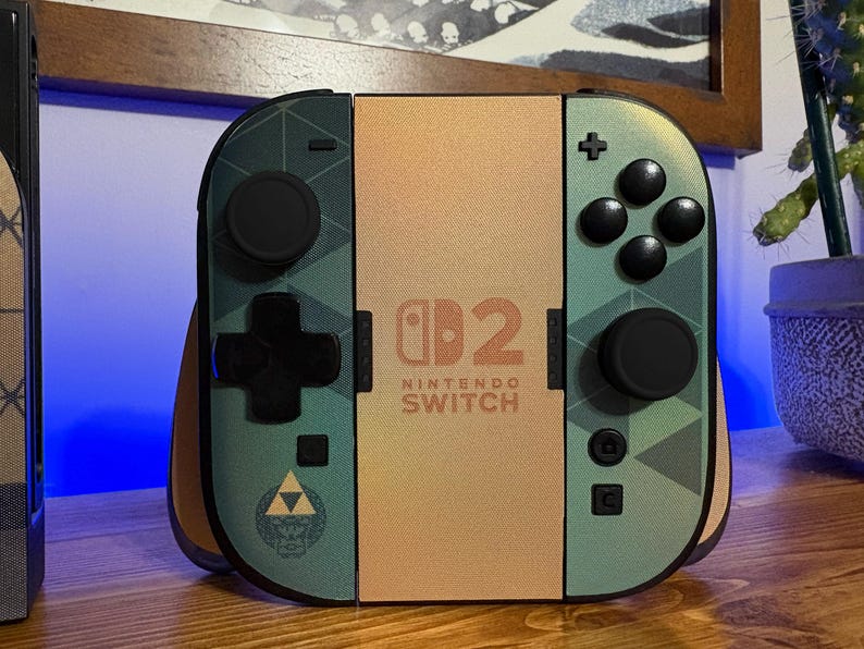 May include: A Nintendo Switch game console controller set featuring a custom skin with a green geometric pattern, black buttons, and a central gold panel displaying the Nintendo Switch logo and the number 2. A Triforce emblem is visible on the left.