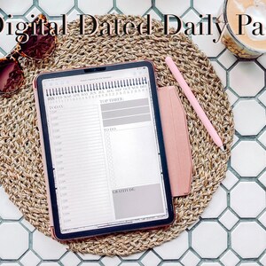 May include: A pink iPad with a digital daily planner app open. The app has a calendar, a to-do list, and a gratitude section. The iPad is on a woven placemat and a pink stylus is next to it.